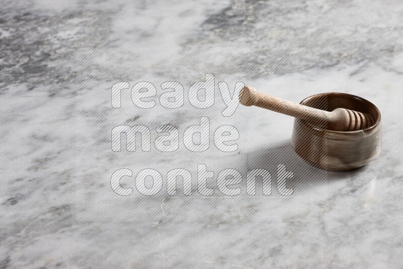 Brown pottery bowl with wooden honey dipper in it on grey marble background