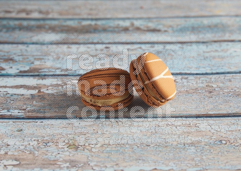 45º Shot of of two assorted Brown Irish Cream, and light brown Almond Cream macarons next to each other on light blue background