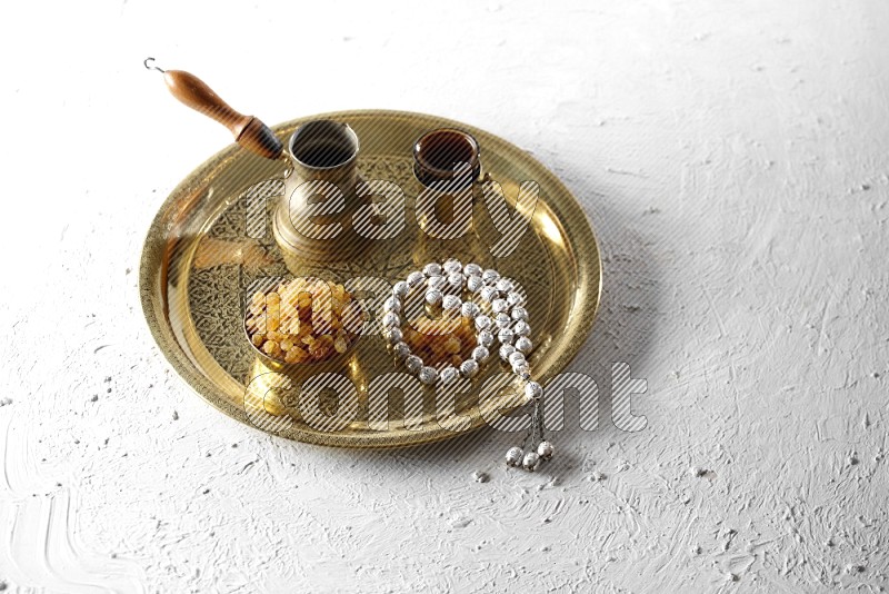 زبيب في وعاء معدني مع قهوة وسبحة على صينية علي خلفية بيضاء