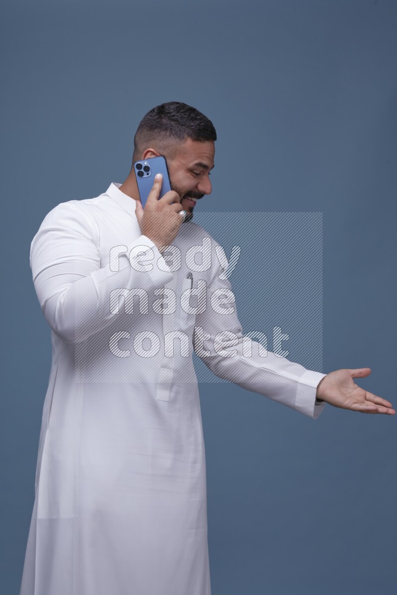 A Saudi man calling on blue background wearing Saudi Thob