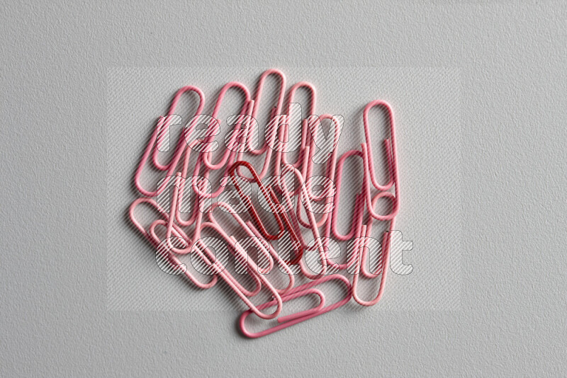 A red paperclip surrounded by bunch of pink paperclips on grey background