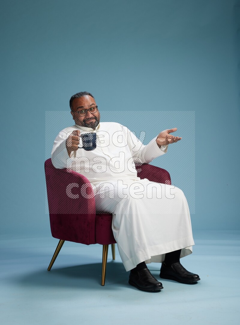 Saudi Man without shimag sitting on chair drinking coffee on blue background