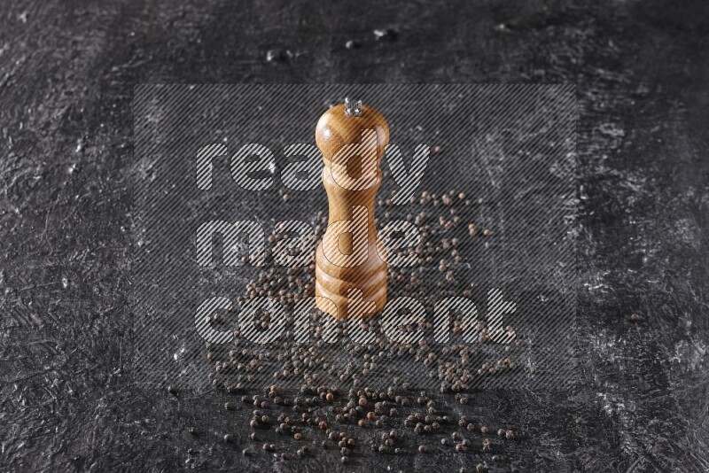 A wooden grinder with black pepper beads on a textured black flooring