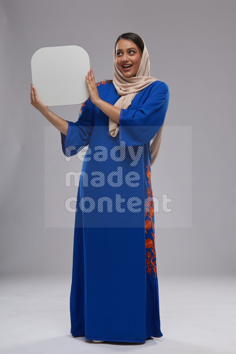 A Saudi woman standing wearing Jalabeya holding a social media sign