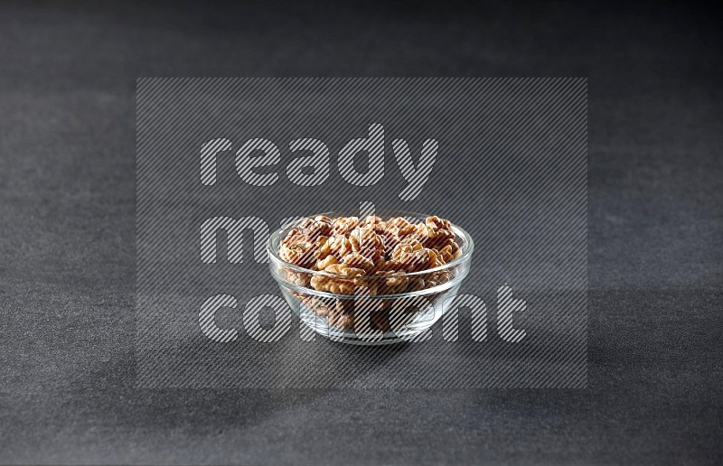 A glass bowl full of peeled walnuts on a black background in different angles
