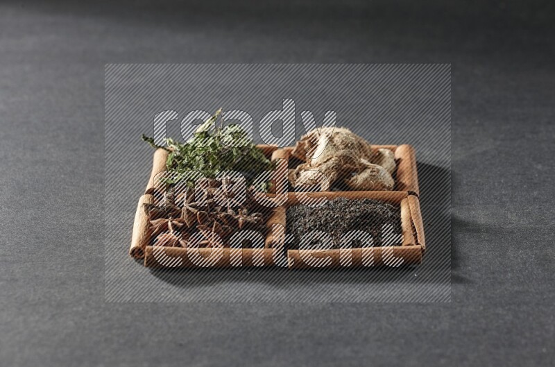 4 مربعات من عيدان القرفة ممتلئة بالشاي الأسود والزنجبيل المجفف والنعناع المجفف واليانسون النجمي على أرضية سوداء