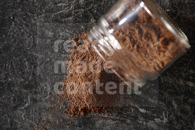 A flipped glass jar full of cloves powder on a textured black flooring