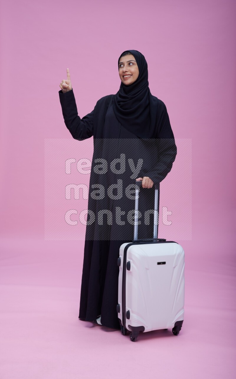 Saudi woman wearing Abaya standing holding bag on pink background