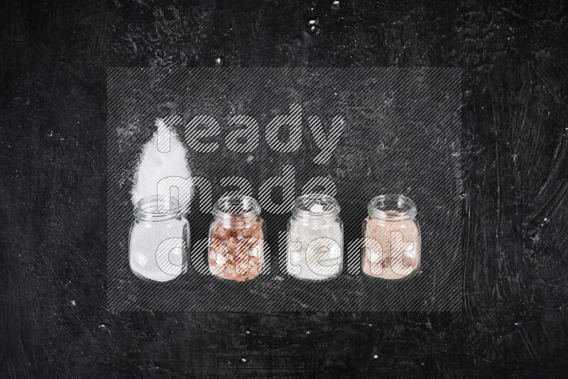 4 glass jars filled with table salt, coarse sea salt, fine himalayan salt and coarse himalayan salt on black background