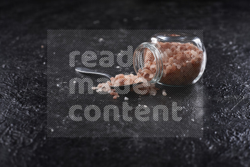 A glass jar full of coarse himalayan salt crystals on black background