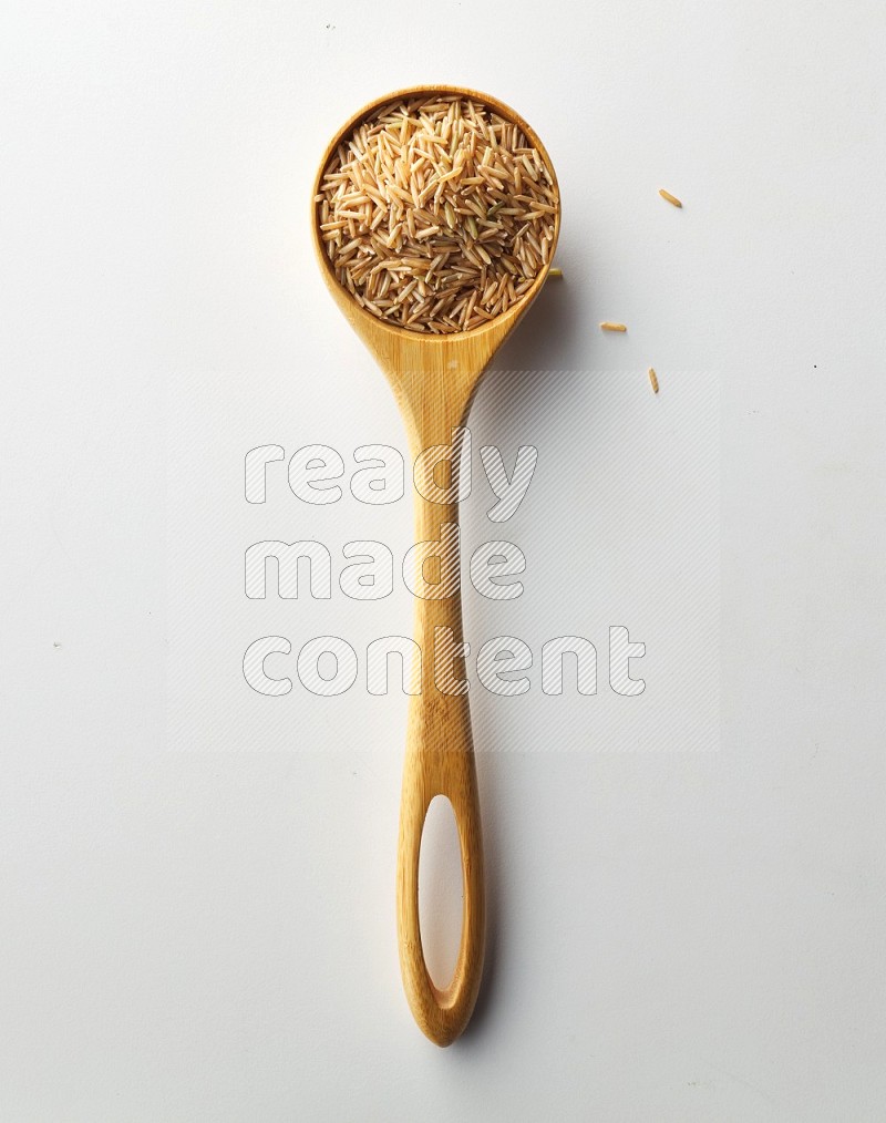 Top-view of a long grain brown rice inside a wooden spoon on white background