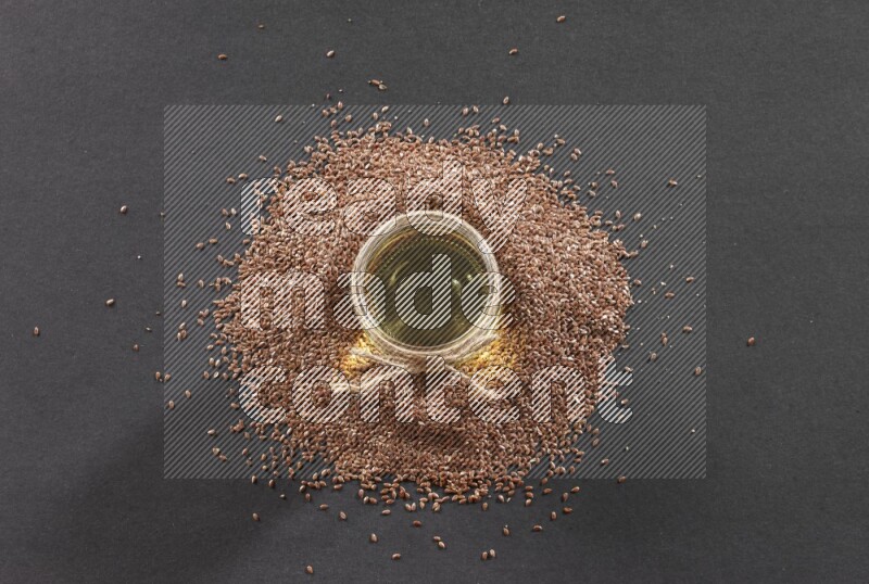 A glass jar full of flaxseeds oil surrounded by the seeds on a black flooring