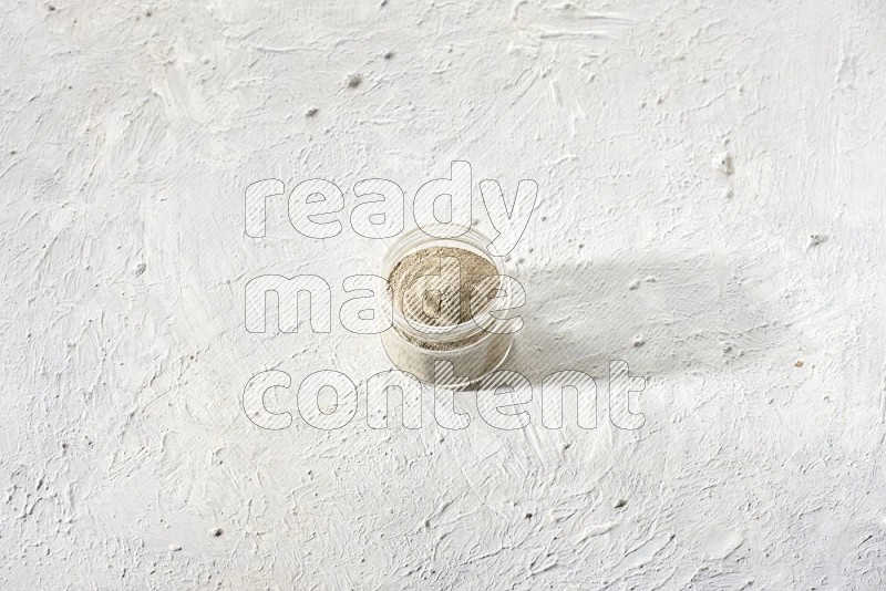 A glass jar full of white pepper powder on textured white flooring
