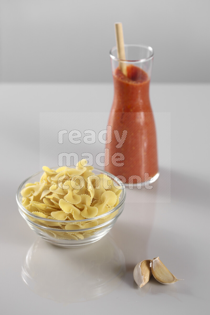Raw pasta with tomatoe pasta with different ingredients such as cherry tomatoes, basil, garlic, bay laurel, cardamom, white pepper, black pepper, red chilis and wheat stalks on light grey background