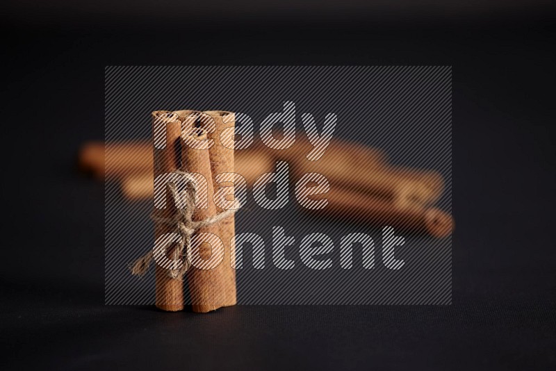 4 Cinnamon sticks stacked and bounded with more sticks in the background on black flooring