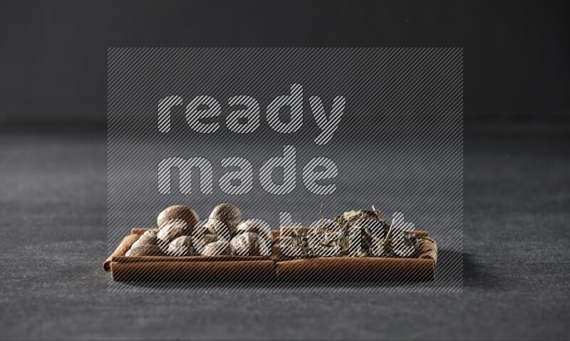 2 squares of cinnamon sticks full of nutmegs and dried basil on black flooring