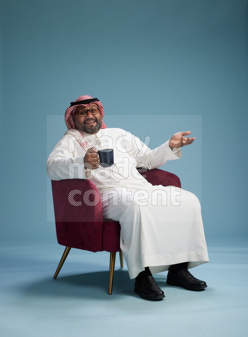 Saudi Man with shimag sitting on chair drinking coffee on blue background