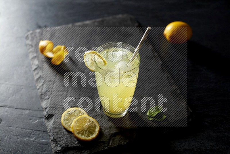 A glass of lemon juice with a straw on black background