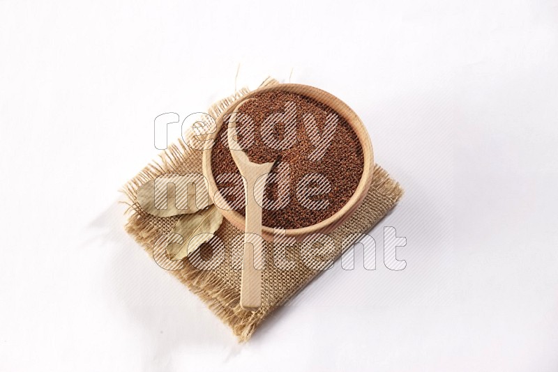 A wooden bowl and spoon full of garden cress seeds on burlap fabric on a white flooring