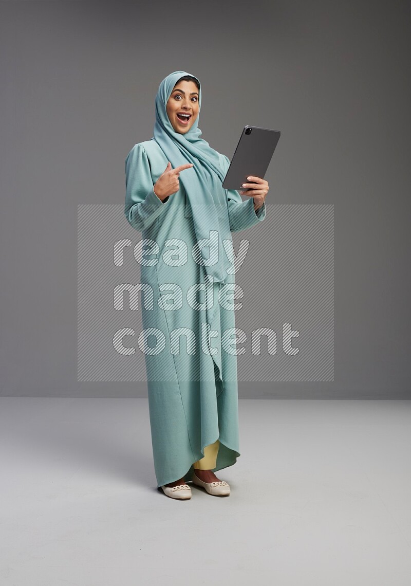 Saudi Woman wearing Abaya standing working on tablet on Gray background