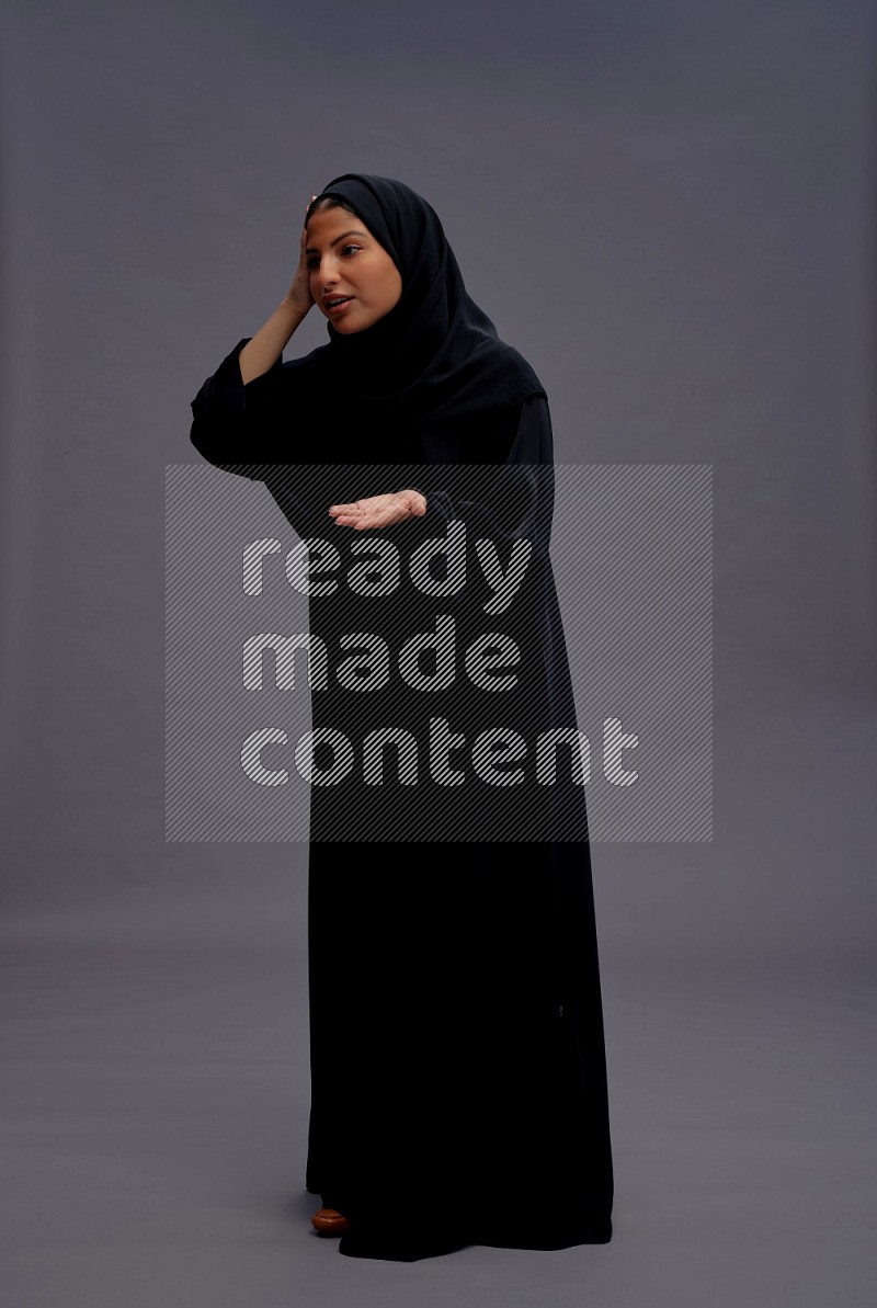 Saudi woman wearing Abaya standing interacting with the camera on gray background