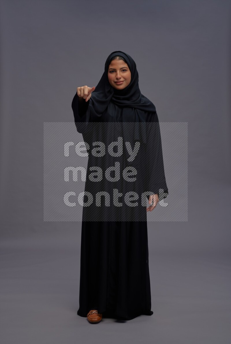 Saudi woman wearing Abaya standing interacting with the camera on gray background