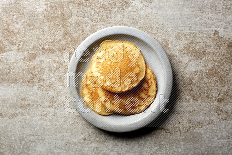 Three stacked plain pancakes in a grey plate on beige background