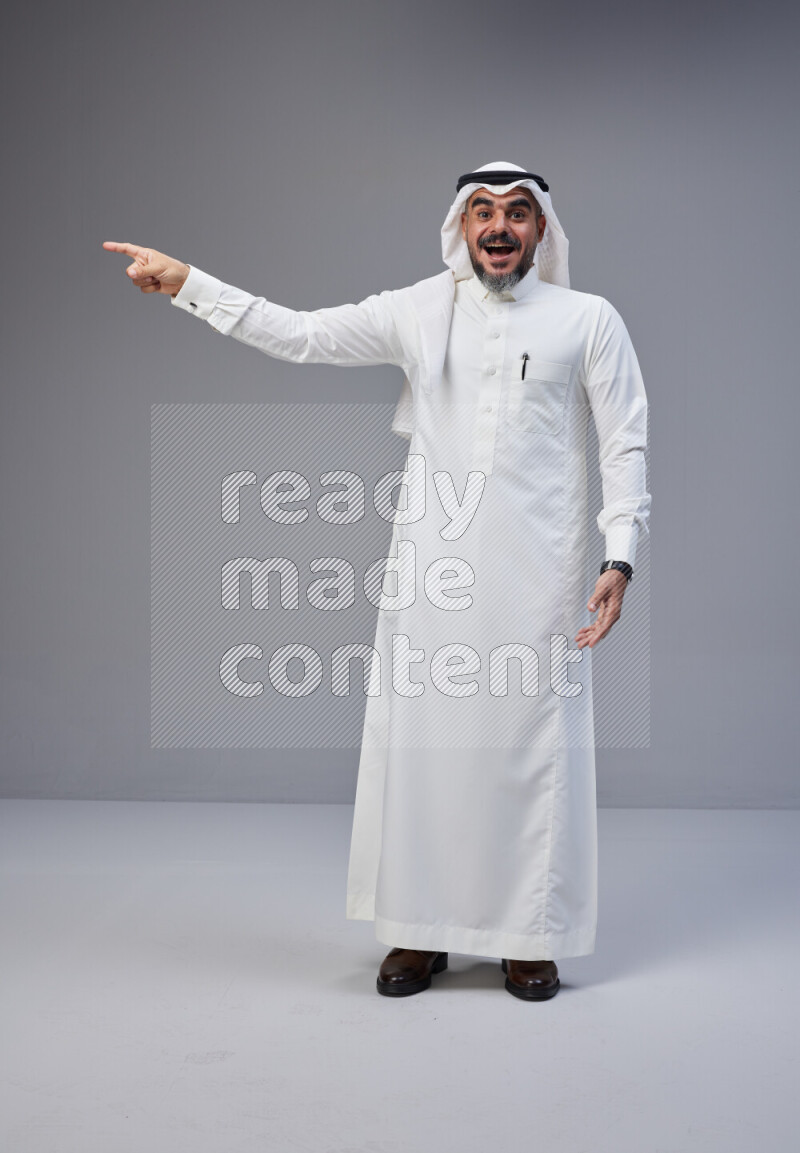 Saudi man Wearing Thob and white Shomag standing interacting with the camera on Gray background
