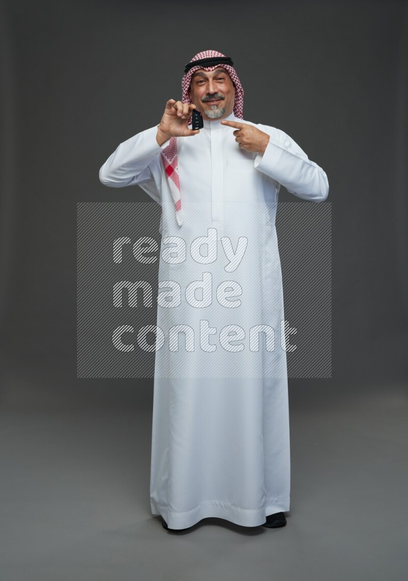 Saudi man with shomag Standing holding car key on gray background