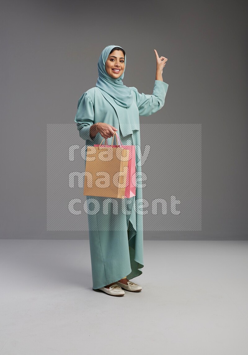 Saudi Woman wearing Abaya standing holding shopping bag on Gray background