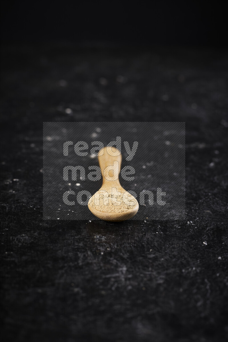 A wooden spoon full of ground ginger powder on black background