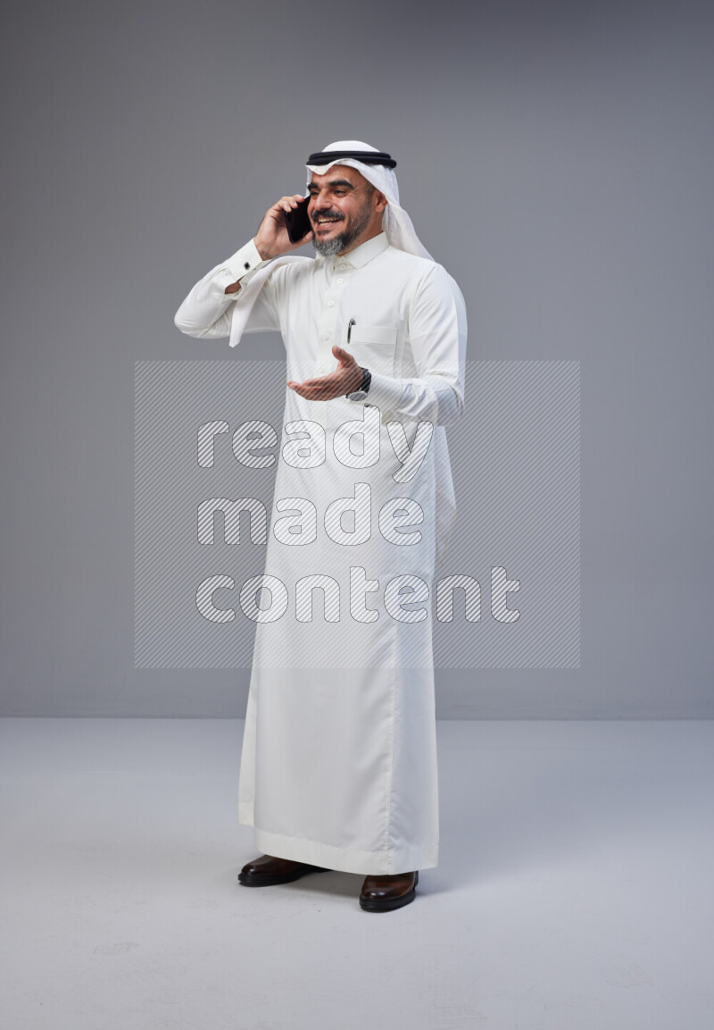 Saudi man Wearing Thob and white Shomag standing talking on phone on Gray background