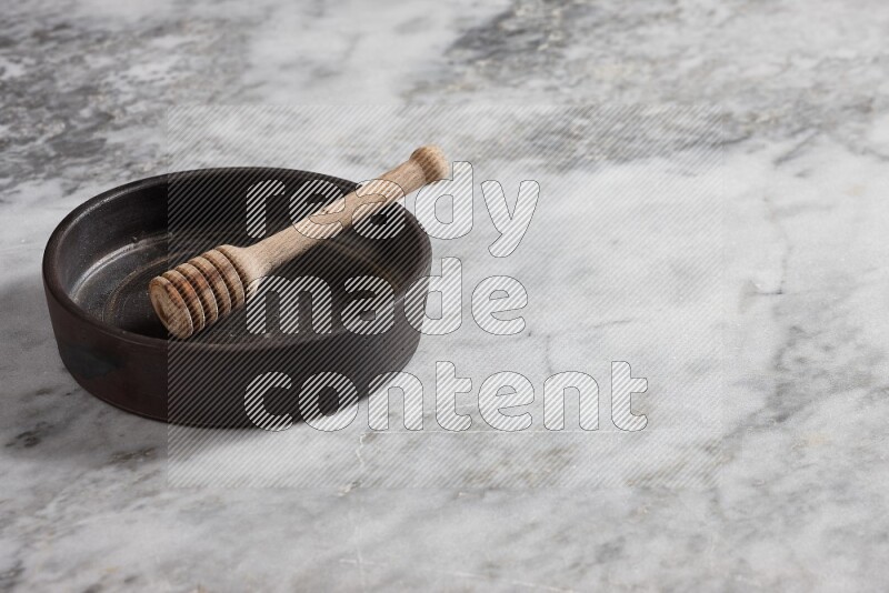 Black pottery oven plate with wooden honey dipper in it on grey marble background