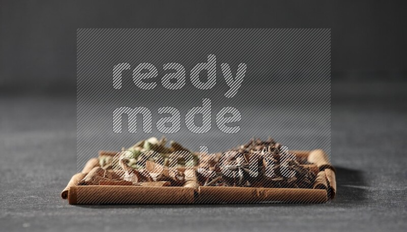 4 مربعات من عيدان القرفة ممتلئة بقطع القرفة وحبوب الهيل والقرنفل اليانسون النجمي على أرضية سوداء