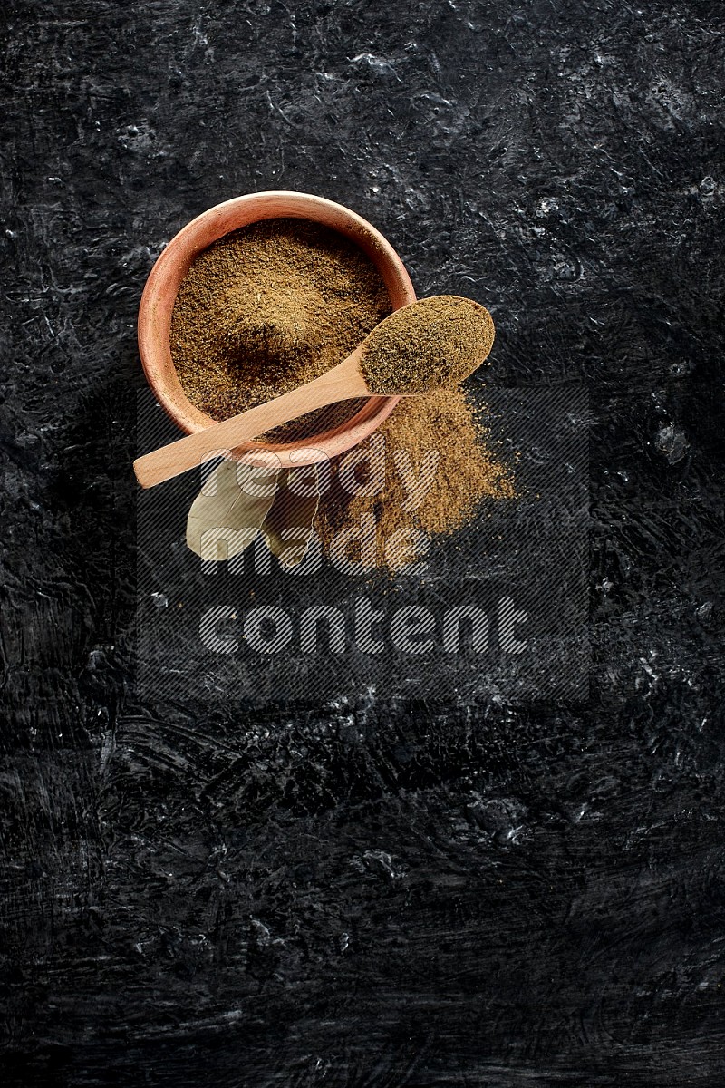 وعاء خشبي وملعقة خشبية مليئتين ببودرة الكمون على أرضية سوداء