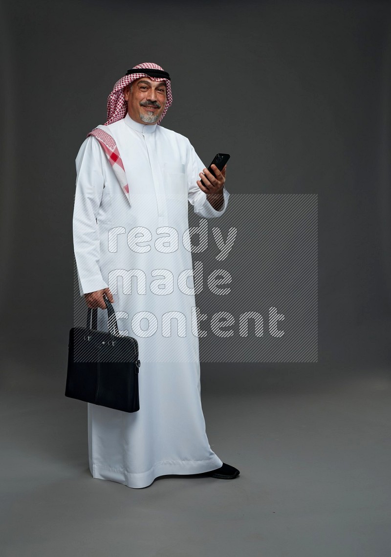 Saudi man with shomag Standing holding bag and phone on gray background