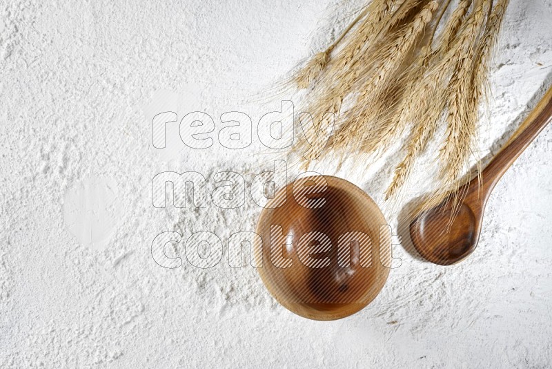 Wheat stalks with a wooden bowl and spoon on flour