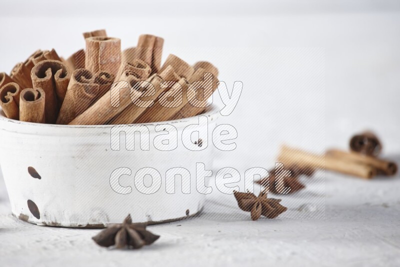 White bowl full of cinnamon sticks surrounded by star anis on a textured white background in different angles