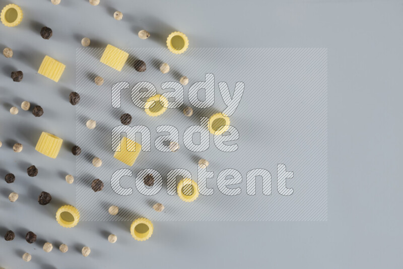 Raw pasta with different ingredients such as cherry tomatoes, garlic, onions, red chilis, black pepper, white pepper, bay laurel leaves, rosemary, cardamom and mushrooms on light blue background