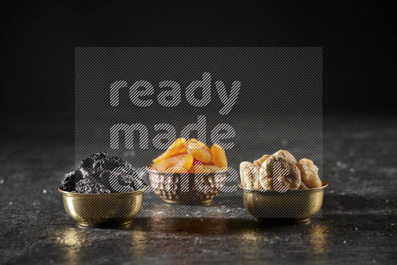 Dried fruits in metal bowls in a dark setup