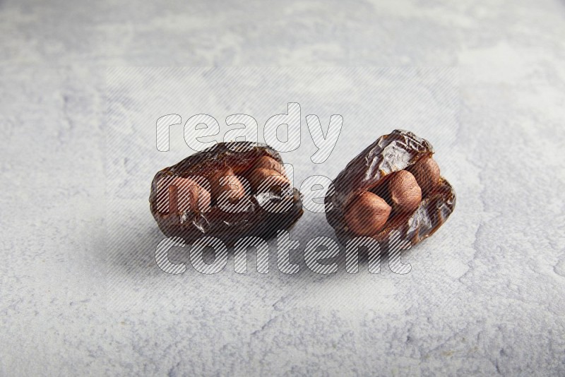 two hazelnuts stuffed madjoul dates on a light grey background