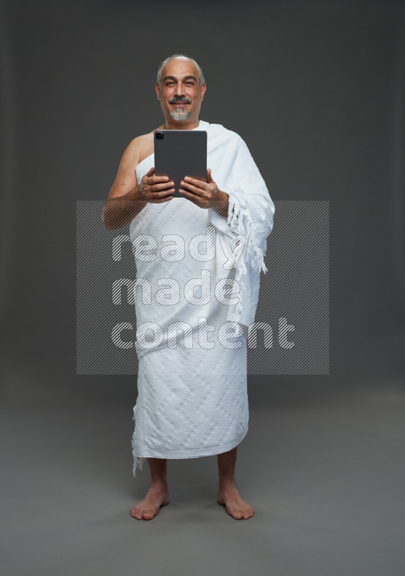 A man wearing Ehram Standing working on tablet on gray background