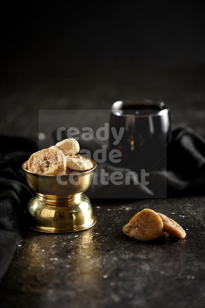 Dried fruits in a metal bowl with tamarind and a napkin in a dark setup