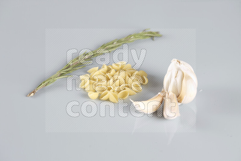 Raw pasta with different ingredients such as cherry tomatoes, garlic, onions, red chilis, black pepper, white pepper, bay laurel leaves, rosemary, cardamom and mushrooms on light blue background