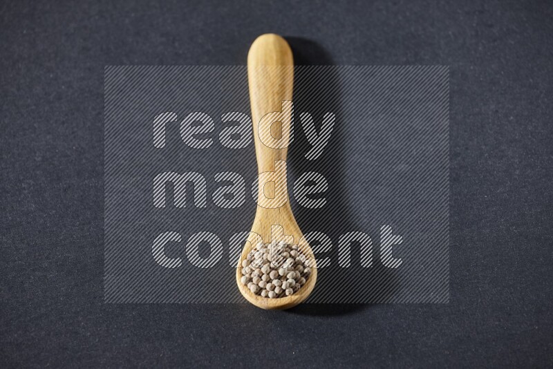 A wooden spoon full of white pepper beads on black flooring