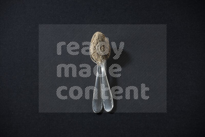 ملعقتان معدنيتان ممتلئتان ببودرة الهيل على خلفية سوداء