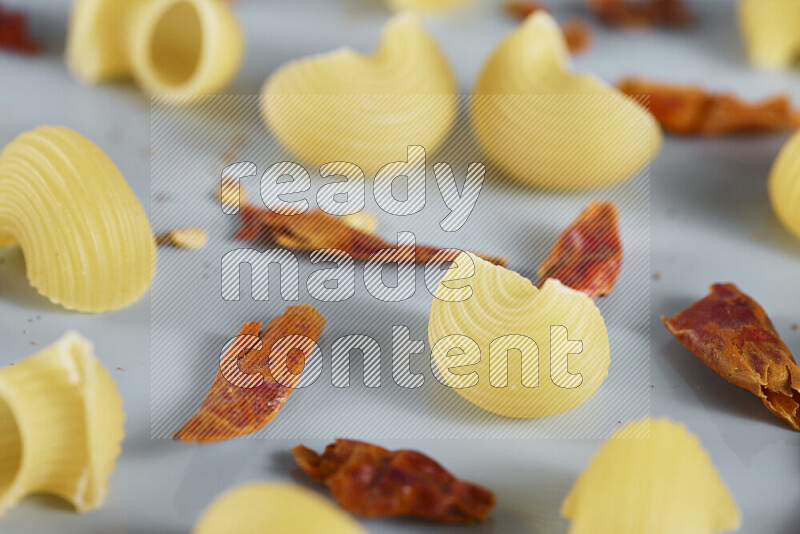 Raw pasta with different ingredients such as cherry tomatoes, garlic, onions, red chilis, black pepper, white pepper, bay laurel leaves, rosemary, cardamom and mushrooms on light blue background