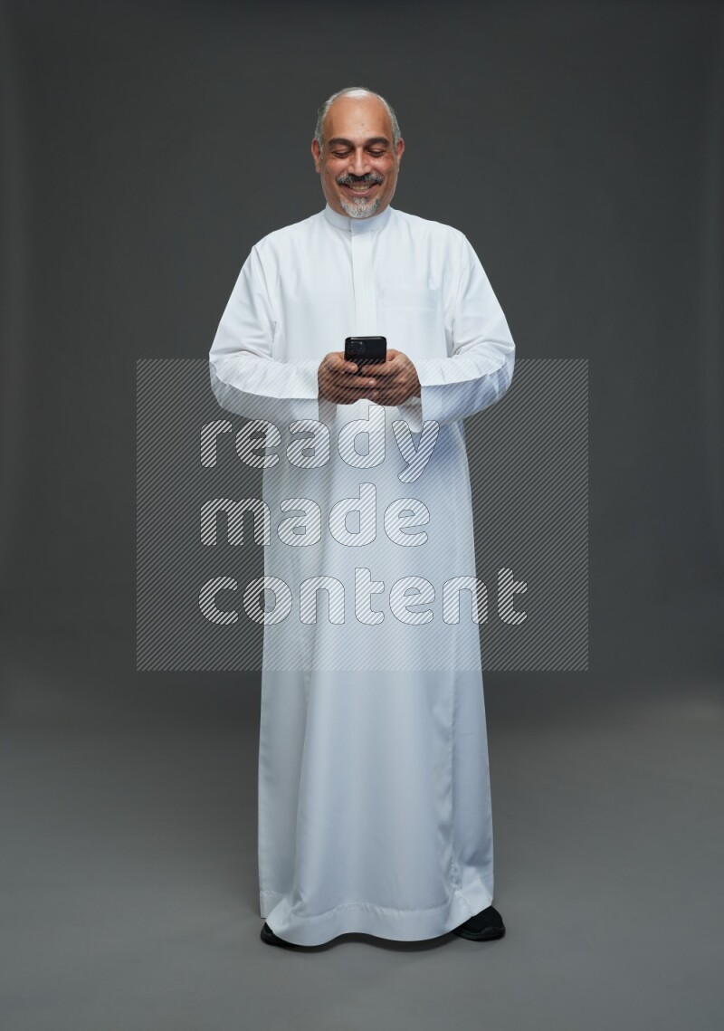 Saudi man without shomag Standing texting on phone on gray background