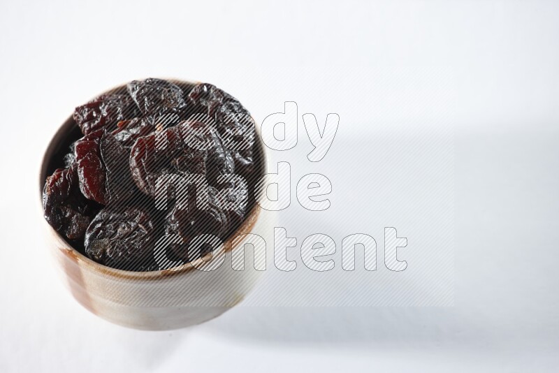 وعاء بيج من السيراميك ممتلئ بالبرقوق المجفف على خلفية بيضاء