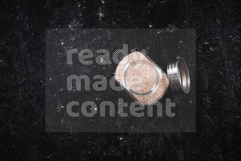 A glass jar full of fine himalayan salt on black background